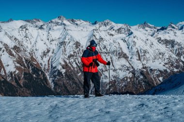 Tourist with backpack and trekking poles walking walking in the snowy mountains at sunny day