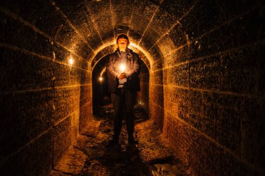 Urban explorer with candle in old vaulted underground tunnel. clipart