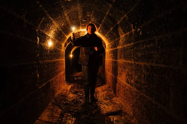 Urban explorer with candle in old vaulted underground tunnel.