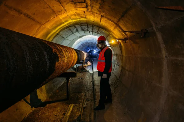 Tunnel worker examines pipeline in underground tunnel.