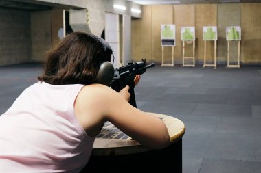 Kulaklıklı bir kız poligonda tüfekle ateş ediyor..
