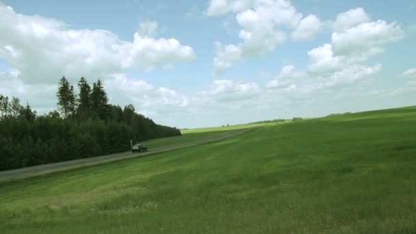 Voitures roulent le long de la prairie verte — Video