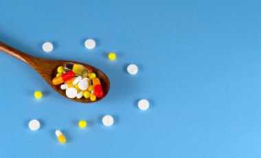Hap, tablet, vitamin, ilaç, omega 3 balık yağı, jel kapsülleri, ilaç ve sağlık hizmetleri için gıda takviyesi dolu tahta kaşık. Mavi arkaplan.