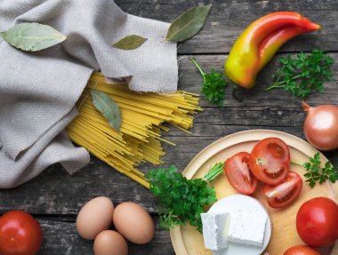 Makarna ve makarna sosu yapmak için malzemeler. Fesleğen, soğan, bıldırcın yumurtası, domates, badem, koyu arkaplanda parmesan peyniri.