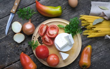 Makarna ve makarna sosu yapmak için malzemeler. Fesleğen, soğan, bıldırcın yumurtası, domates, badem, koyu arkaplanda parmesan peyniri.