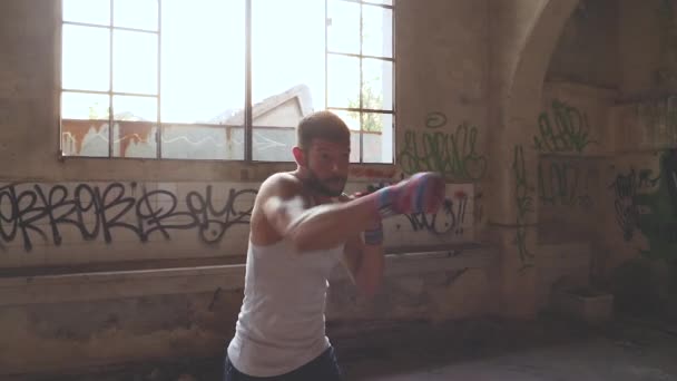 Boxeador masculino haciendo ejercicio de boxeo en la sombra en un viejo edificio abandonado — Vídeo de stock