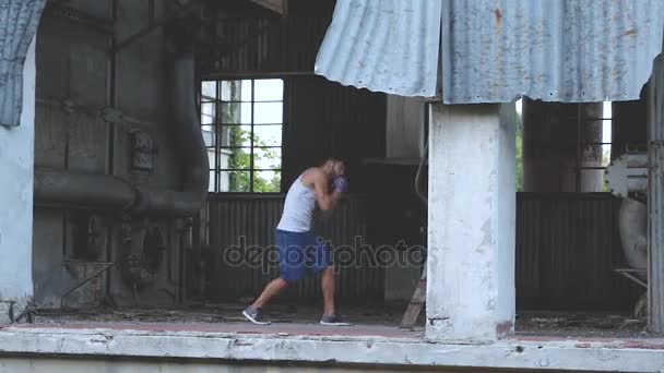 Boxeador masculino haciendo ejercicio de boxeo en la sombra en una vieja fábrica abandonada — Vídeo de stock