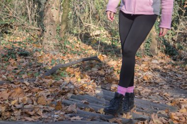 Doğada sağlıklı bir hayat, sportif giyimli genç bir kadın yürüyüş yapıyor, kerestelerden yapılmış küçük bir köprüden geçiyor.