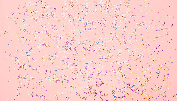 Разноцветные конфетти блестки на розовом фоне — стоковое фото