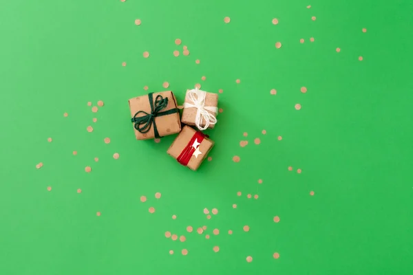 Three handcraft gifts on green background with confetti — Stok fotoğraf