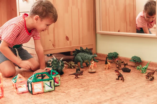 快乐的男孩在儿童房里与玩具恐龙和磁力建设者玩耍 — 图库照片