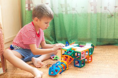 Anaokulu öğrencisi evde oynuyor. Manyetik yapıcıyla yerde oturuyor..