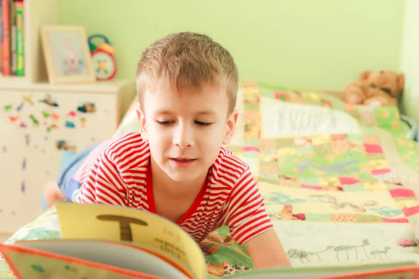 Un enfant lit un bol couché sur son lit — Photo