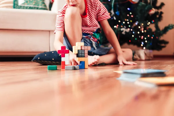 Ein Junge sitzt auf dem Boden in der Nähe eines Weihnachtsbaums und spielt ein Make-and-Break-Spiel. — Stockfoto