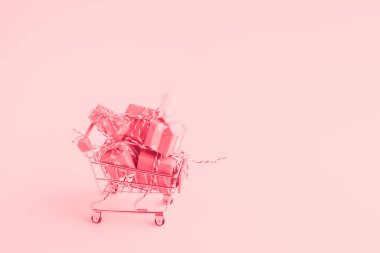 Trolley alışveriş arabası arka planda bir sürü kağıda sarılı hediye kutusuyla dolu. Pembe tonlu.