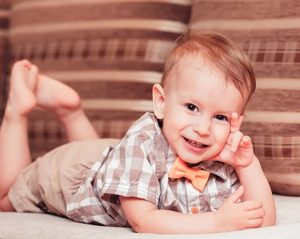 Tシャツを着た2歳の男の子と、お腹の上に寝そべって笑っている蝶ネクタイ — ストック写真