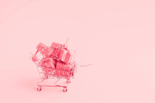 Wagen winkelwagen gevuld met veel papier verpakt geschenkdozen op een lichte achtergrond. getint met roze kleur. — Stockfoto