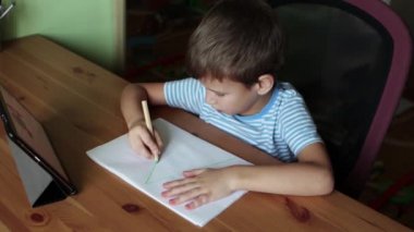 Sevimli çocuk, karantina sırasında evde eğitim ve tablet kullanarak A harfi yazıyor.