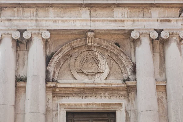 Massonic eye sign inside triangle on building of Church of St. Magdalena, Canaregio District, Venice, Italy. Text on portal above entrance in Latin means: Wisdom has built a house