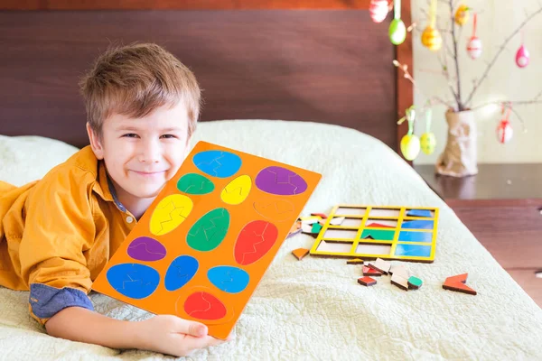 快乐的男孩以复活节彩蛋的形式在家里展示着现成的拼图 背景中的复活节装饰 — 图库照片