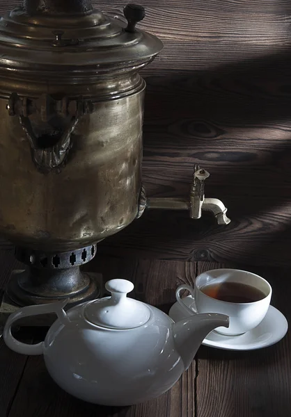 Šálek čaje, bílou konvici a starý samovar na tmavý dřevěný stůl — Stock fotografie