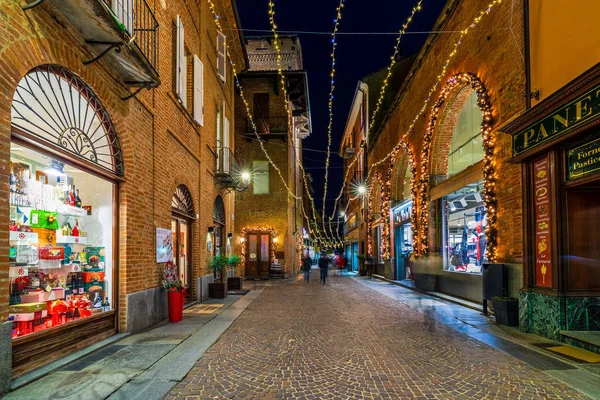 İtalya, Alba 'da Noel aydınlatmasıyla süslenmiş dar kaldırım taşı caddesi ve dükkanlar. — Stok fotoğraf