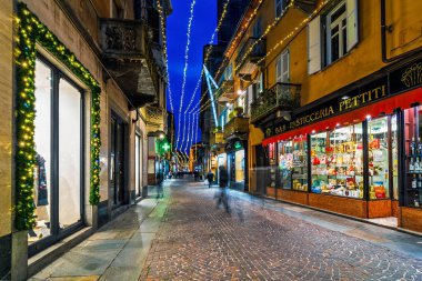 Alba, İtalya 'da Noel aydınlatmasıyla süslenmiş kaldırım taşı caddesi ve dükkanlar.