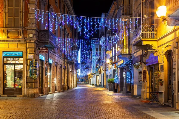 Shops on evening cobblestone street decorated with Christmas lights in Alba, Italy. — Stockfoto