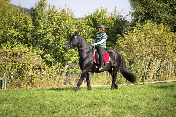 Piękna młoda kobieta jeździ jej czarny koń — Zdjęcie stockowe
