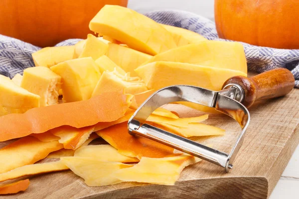 Peeled pumpkin and peeler on wooden board — Stock Photo, Image