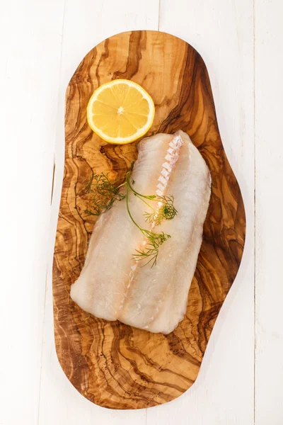 Eglefino crudo con aneto e limone su una tavola di legno — Foto Stock