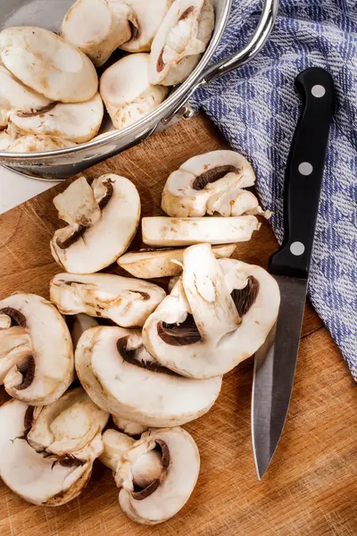 Champignons in Scheiben geschnitten mit Küchenmesser auf einem Holzbrett — Stockfoto