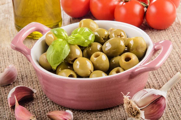 Green olive in a pink bowl, garlic, tomatoes and olive oil in a — Stock Photo, Image