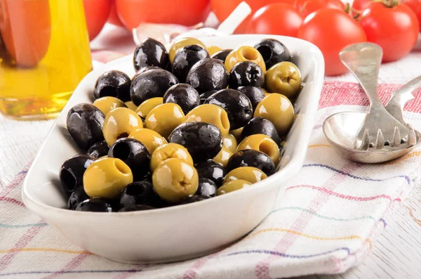 Green and black olives in a bowl, tomatoes and olive oil in the — Stock Photo, Image
