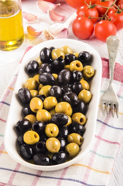 Bol blanc aux olives huileuses vertes et noires, fond tomate , — Photo