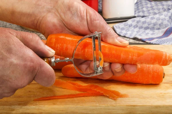 Senior female chef is peeling a fresh carrot — Stock Photo, Image