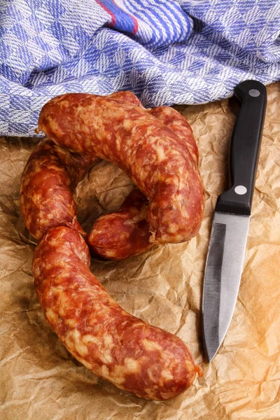 Smoked sausage with knife on brown paper — Stock Photo, Image