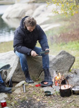 Kamp alanında kayanın üzerinde otururken yemek adam