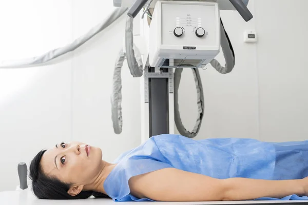 Жіночий пацієнт лежить під рентгенівським пристроєм в оглядовій кімнаті — стокове фото