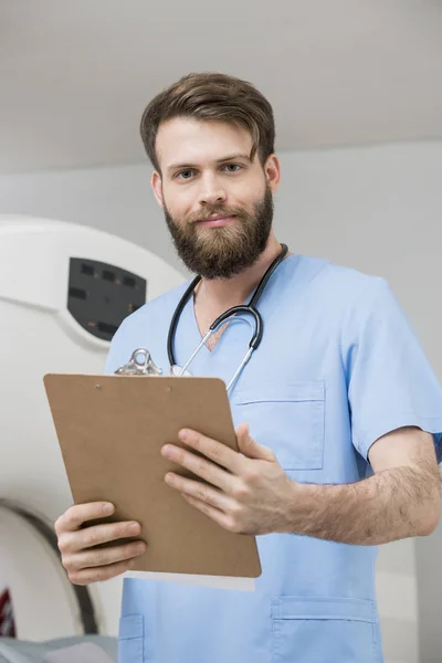 Confiante jovem médico masculino com área de transferência na sala de exame — Fotografia de Stock