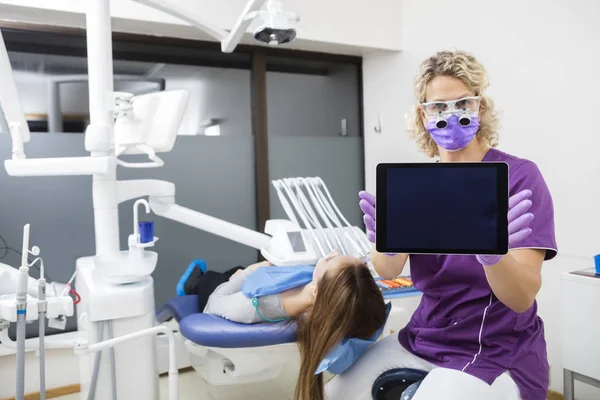 Dentista mostrando computador tablet com tela em branco pelo paciente — Fotografia de Stock