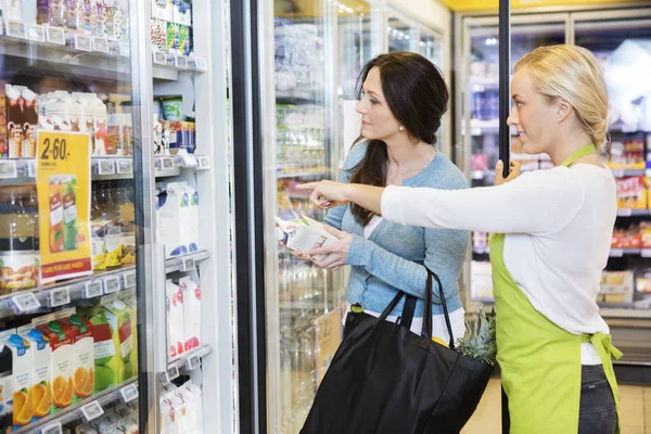 Vendedora mostrando productos a cliente femenino en refrigerador —  Fotos de Stock