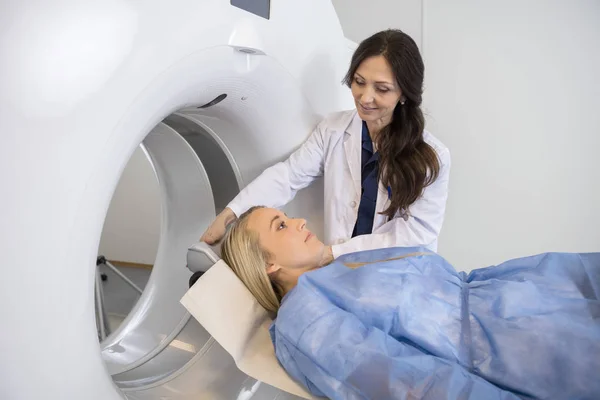 Doctor Preparing Female Patient For MRI Scan In Hospital