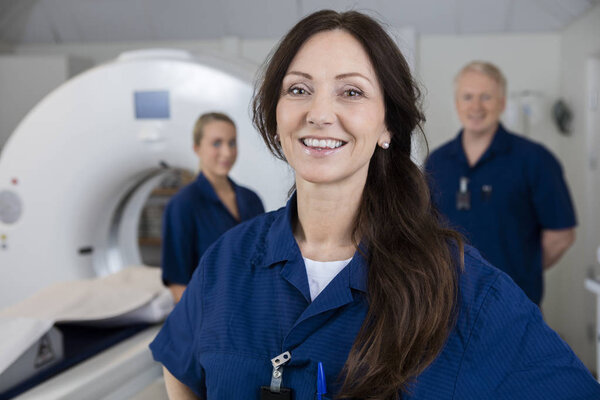 Smiling Female Radiologist With Colleagues Standing By MRI Machi