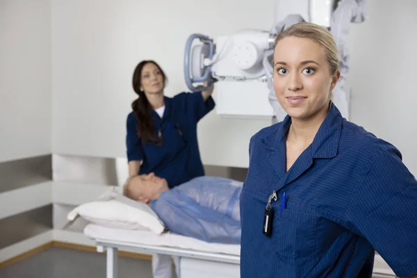 Junge Radiologin steht, während Kollegin Patienten röntgt — Stockfoto