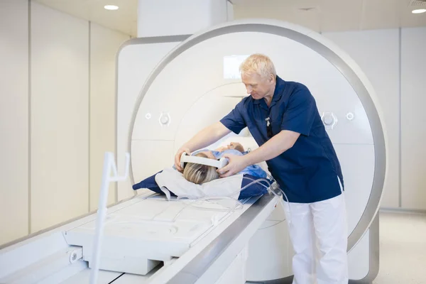 Radiologista colocando fones de ouvido na ressonância magnética paciente submetendo — Fotografia de Stock