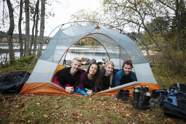 Lächelnde junge Freunde liegen im Zelt am Seeufer — Stockfoto