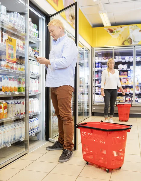 Kundin benutzt Handy am Kühlschrank im Supermarkt — Stockfoto