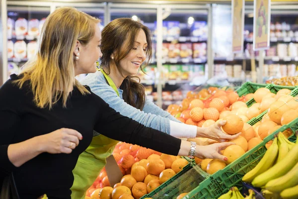 Cliente e vendedora escolhendo laranjas frescas no supermercado — Fotografia de Stock
