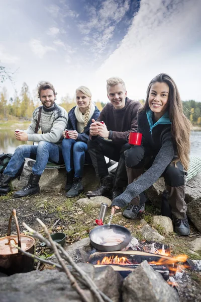 女の湖畔で友達とキャンプファイヤーの上に食べ物を料理 — ストック写真